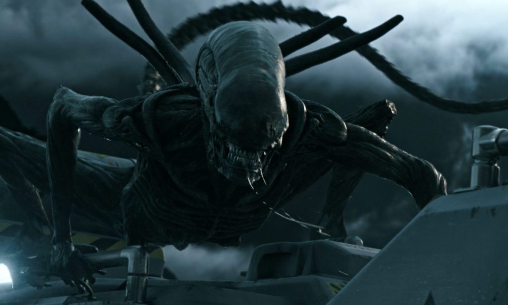 Une créature extraterrestre menaçante, ressemblant à un alien, se tortillant sur une surface métallique sous un ciel nuageux.