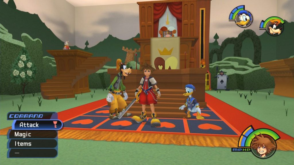 Capture d'écran de Kingdom Hearts 1.5 montrant Sora, Donald et Dingo dans un espace de jeu coloré avec des éléments de design inspirés de Disney. Sora se tient au centre, tenant sa clé, avec un tapis représentant des cœurs en dessous. En arrière-plan, une scène avec une estrade décorée et des arbres stylisés.