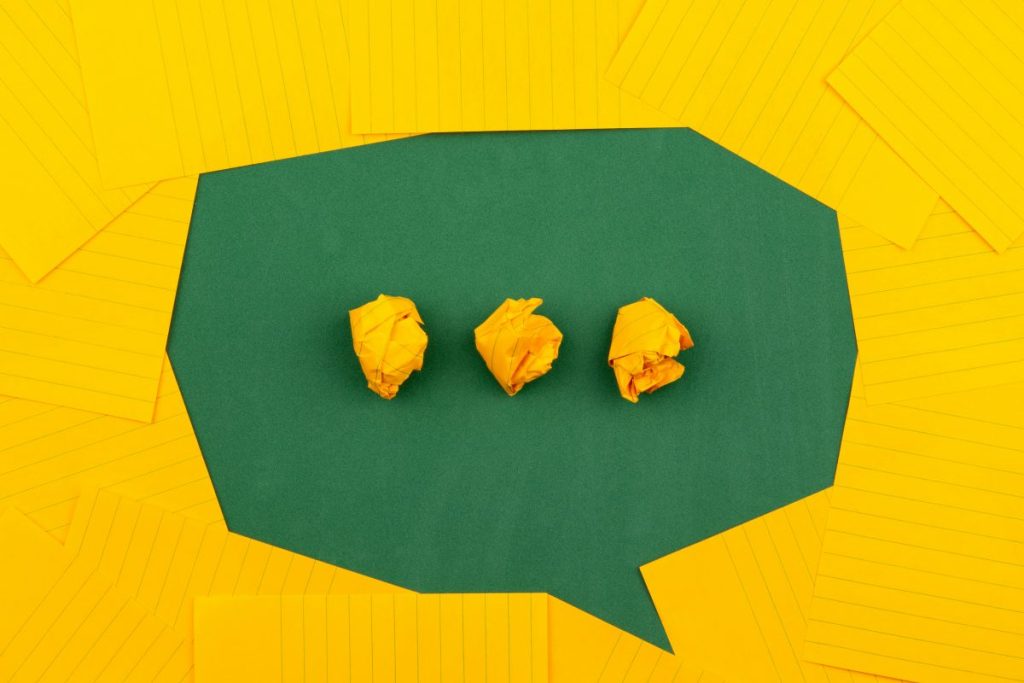 Trois boulettes de papier jaune sur un fond vert en forme de bulle de dialogue, entourées de feuilles de papier jaune.