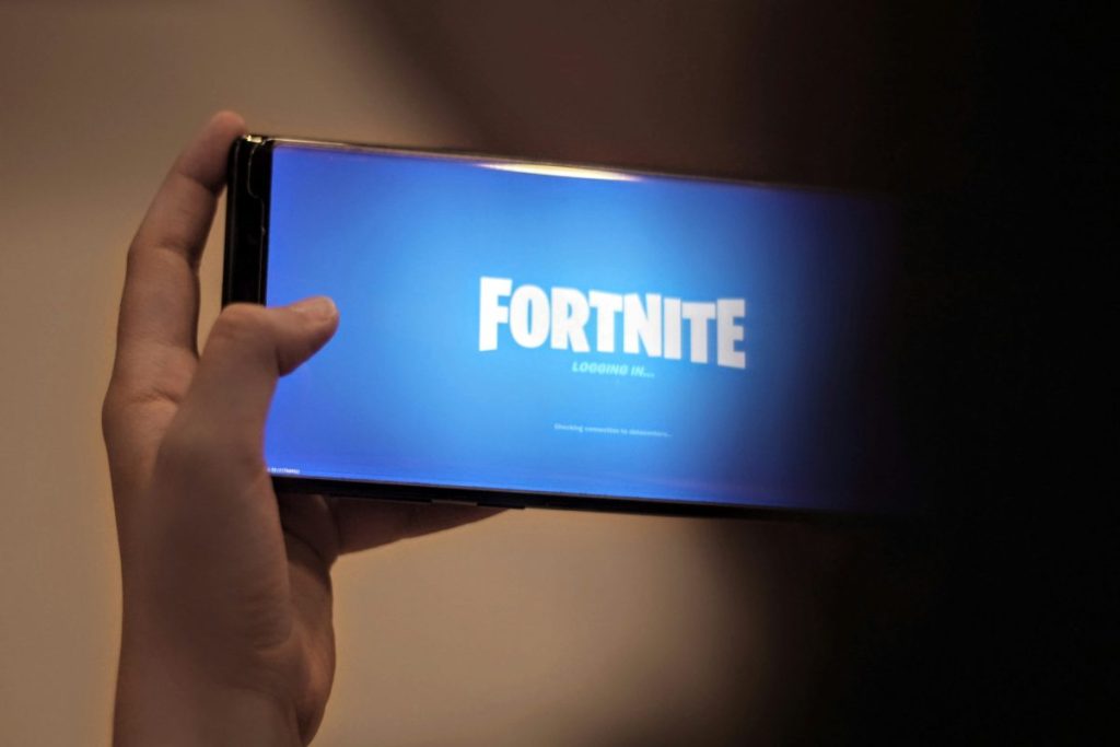 Une main tenant un smartphone affichant l'écran de connexion du jeu Fortnite.