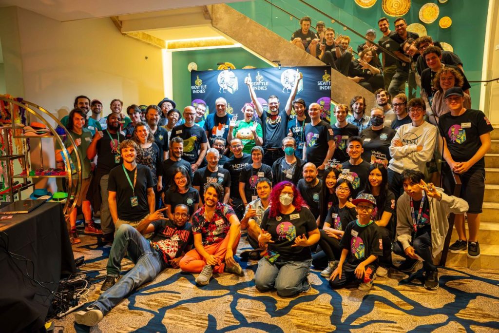 Groupe de personnes posant ensemble lors d'un événement Seattle Indies, avec des affiches en arrière-plan, tous portant des t-shirts noirs.