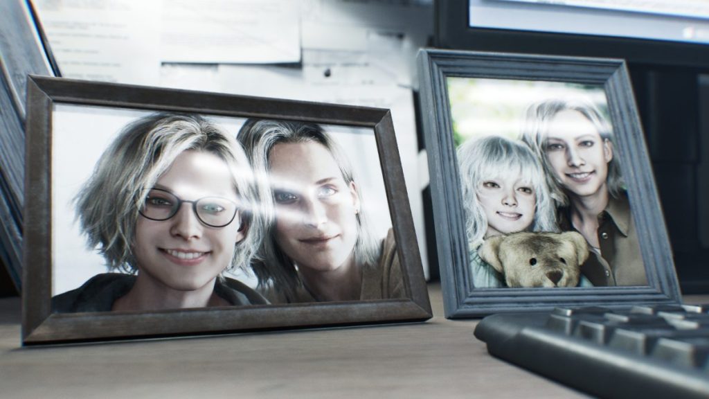 Deux cadres photo posés sur un bureau, l'un montrant une personne avec des lunettes souriante et l'autre un groupe de personnes avec des cheveux clairs et un ours en peluche.