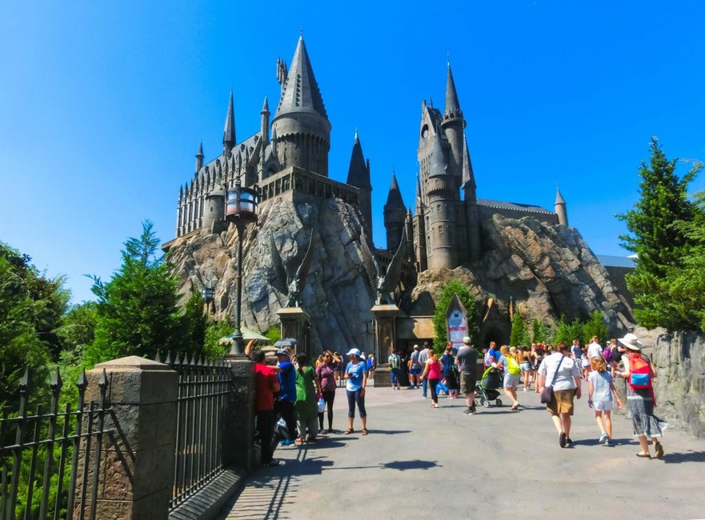 Vue de l'extérieur du château entouré de visiteurs dans un parc d'attractions par une journée ensoleillée.