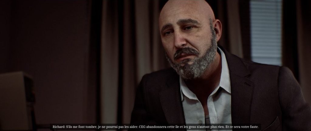 Un homme d'âge moyen avec une barbe et des cheveux chauves, portant un costume sombre, écoute attentivement et parle avec une expression sérieuse dans un environnement intérieur.